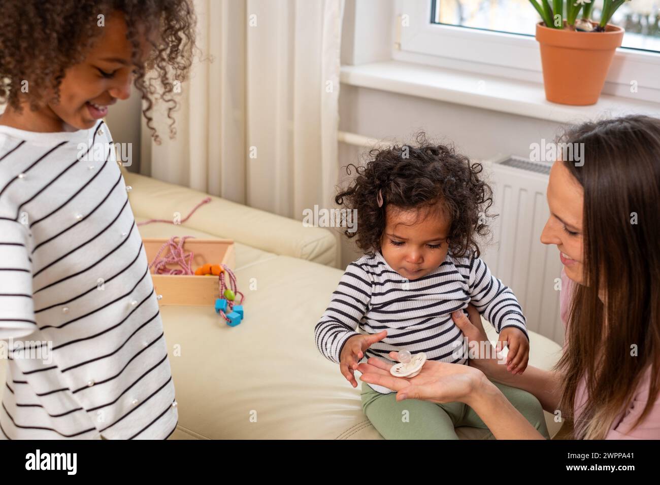 Une mère et ses deux enfants partagent un moment confortable sur un canapé, avec des jouets éparpillés, exsudant la chaleur familiale et les joies de la petite enfance, jouet le Banque D'Images
