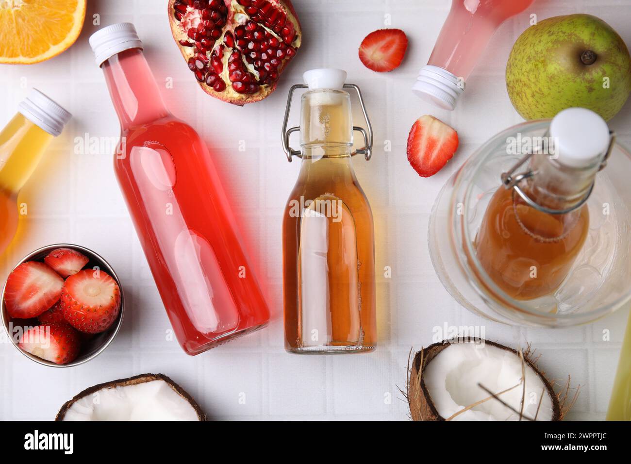 Savoureux kombucha dans des bouteilles en verre et fruits frais sur table carrelée blanche, pose à plat Banque D'Images