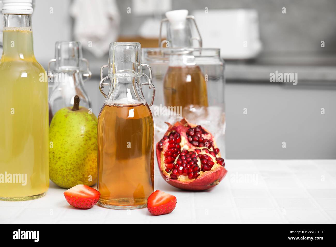 Savoureux kombucha dans des bouteilles en verre et fruits frais sur une table carrelée blanche, espace pour le texte Banque D'Images