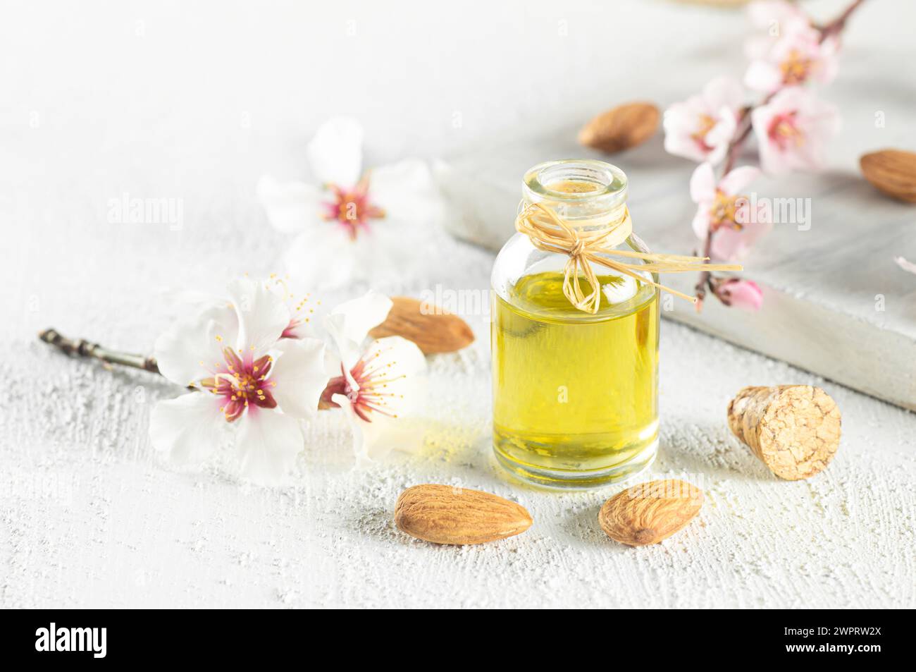 Bouteille en verre d'huile d'amande et noix d'amande , amandes avec fleurs d'amandier sur table. Concept de fond d'amande avec espace de copie Banque D'Images