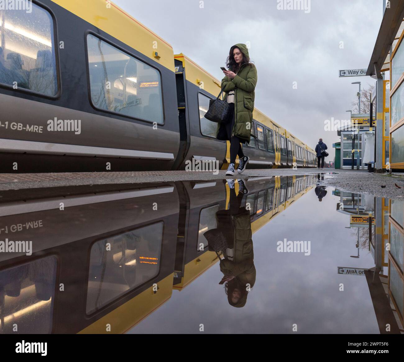 Passager embarquant dans un train Merseyrail Stadler classe 777 à la gare de Bebington reflété dans une flaque sur le quai de la gare Banque D'Images