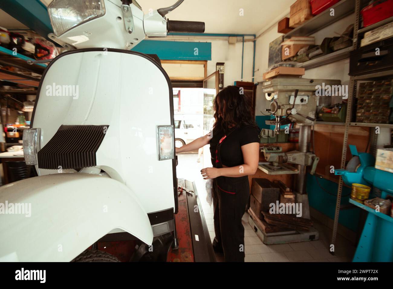 Vue de côté d'un mécanicien faisant un travail de précision sur un scooter vintage, femme latino dans le concept traditionnel des emplois masculins, pouvoir féminin dans la vraie vie Banque D'Images