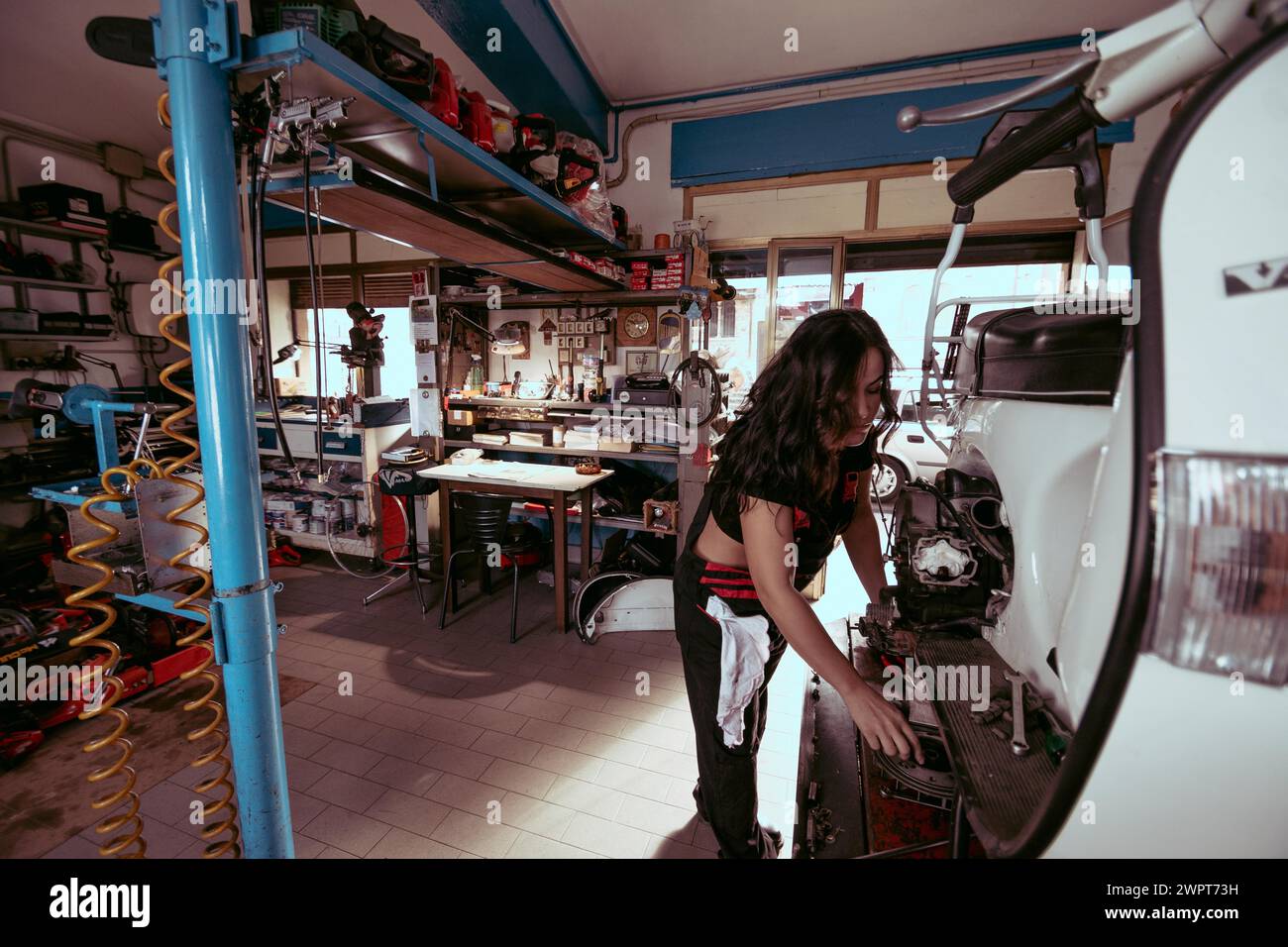 Vue d'une jeune femme brune hispanique aux cheveux longs mécanicien travaillant diligemment dans un atelier emballé sur un scooter, femme latino en traditionnel Banque D'Images