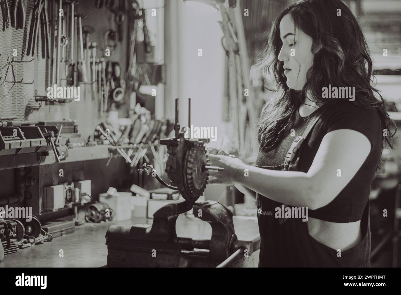 Femme se concentrant sur le travail mécanique sur un banc d'atelier, de vraies femmes exécutant des emplois traditionnels d'homme du passé, photographie en noir et blanc Banque D'Images