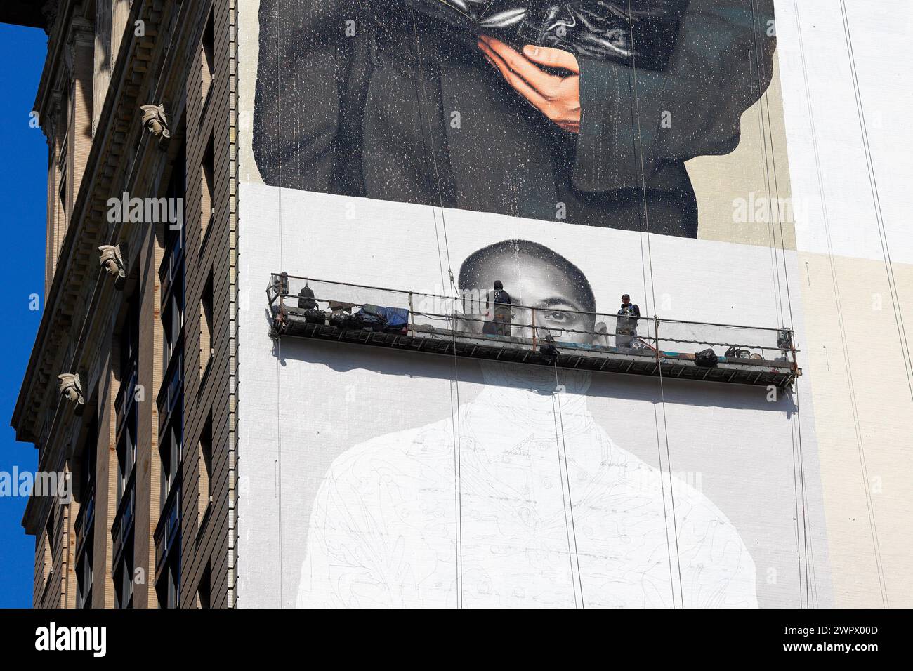 Artistes commerciaux, peintres sur un échafaudage suspendu à la main peignant un panneau publicitaire sur le côté d'un immeuble de grande hauteur à New York. Banque D'Images