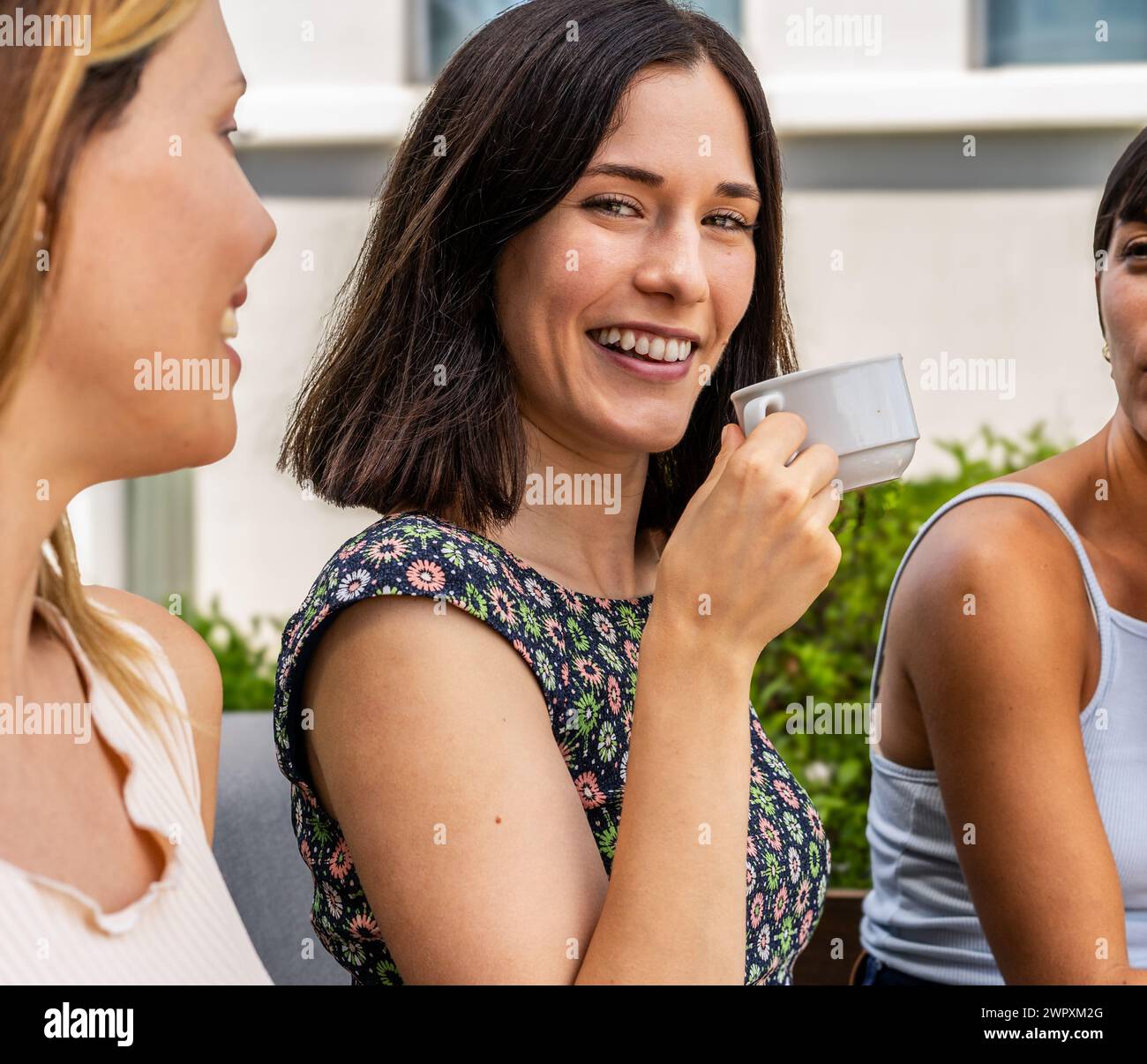Trois femmes sont assises ensemble et l'une d'elles tient une tasse. La femme avec la coupe est souriante et regarde la caméra et les deux autres femmes Ar Banque D'Images