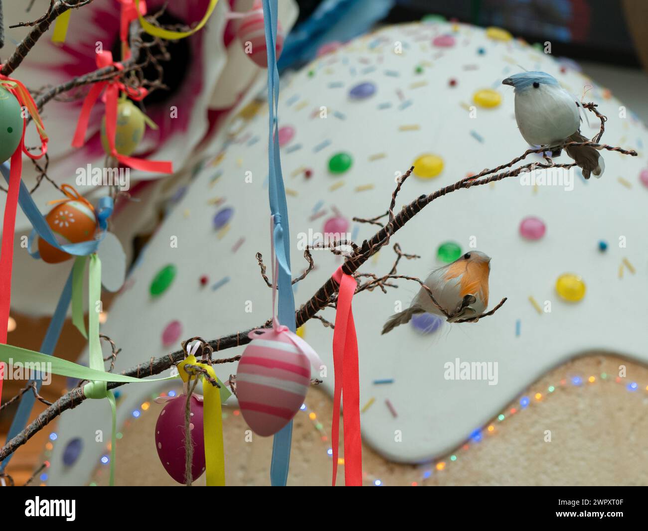 Oeufs décorés suspendus à une branche d'arbre avec des rubans multicolores et des oiseaux assis, foyer sélectif Banque D'Images