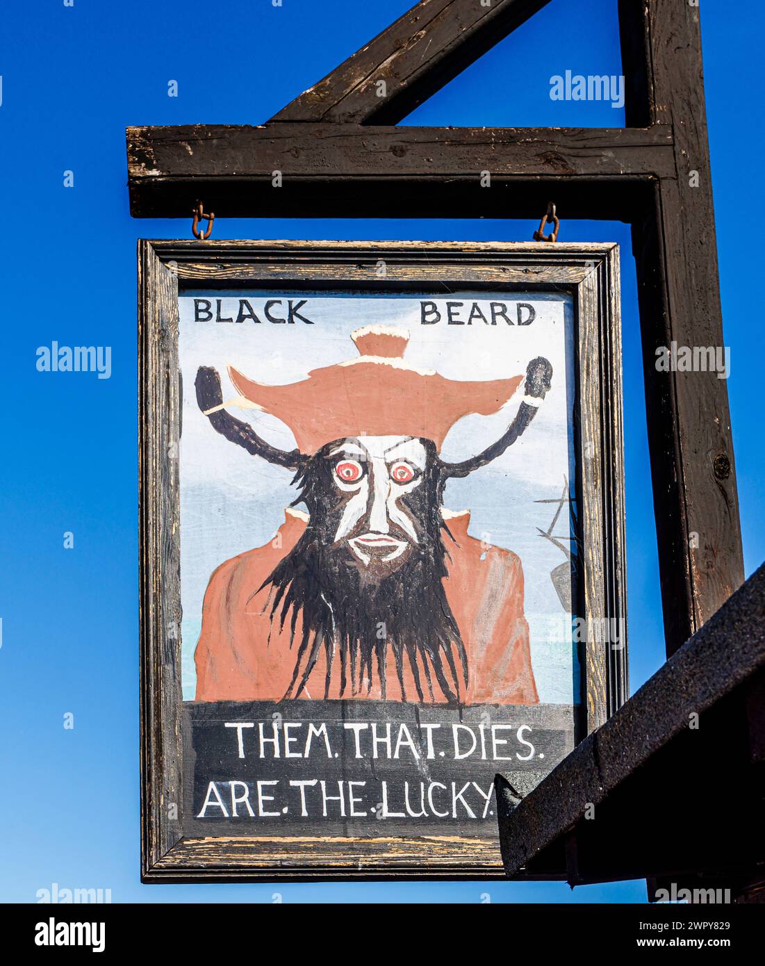 Amusant signe peint en bois avec Barbe Noire et 'Them that dies are the Lucky Ones' dans le stade de la vieille ville de Hastings, East Sussex, Angleterre Banque D'Images