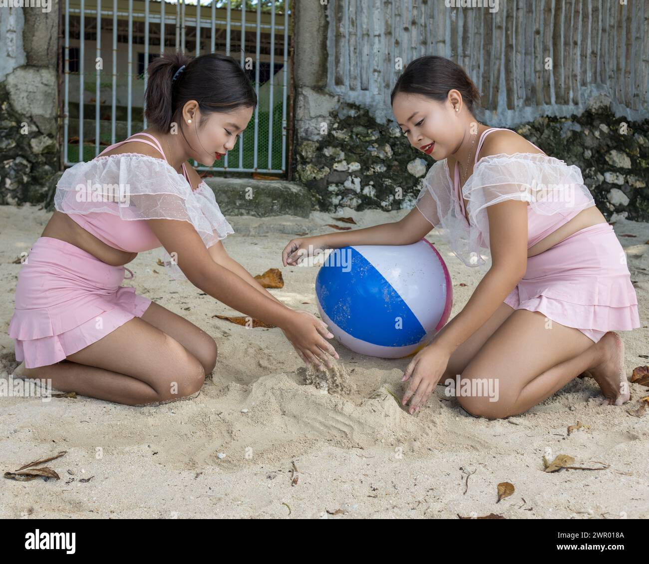 Deux femmes s'agenouillent sur le sable, jouant avec un ballon de plage et des pelures de banane Banque D'Images
