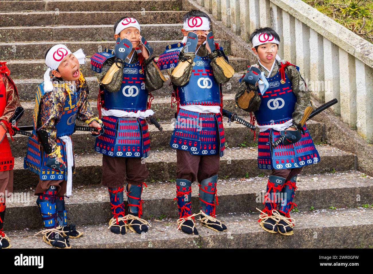 Quatre jeunes garçons japonais vêtus des uniformes de soldats médiévaux Teppou-ashigaru debout sur des marches de pierre faisant des visages. Défilé des samouraïs Tatsuno. Banque D'Images