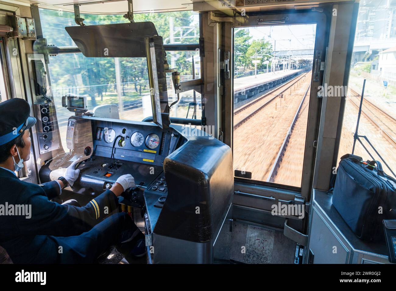 Vue de face à travers la cabine du conducteur d'un train de banlieue avec le conducteur conduisant alors qu'il accélère à travers une gare de la ligne JR Kobe au Japon. Banque D'Images