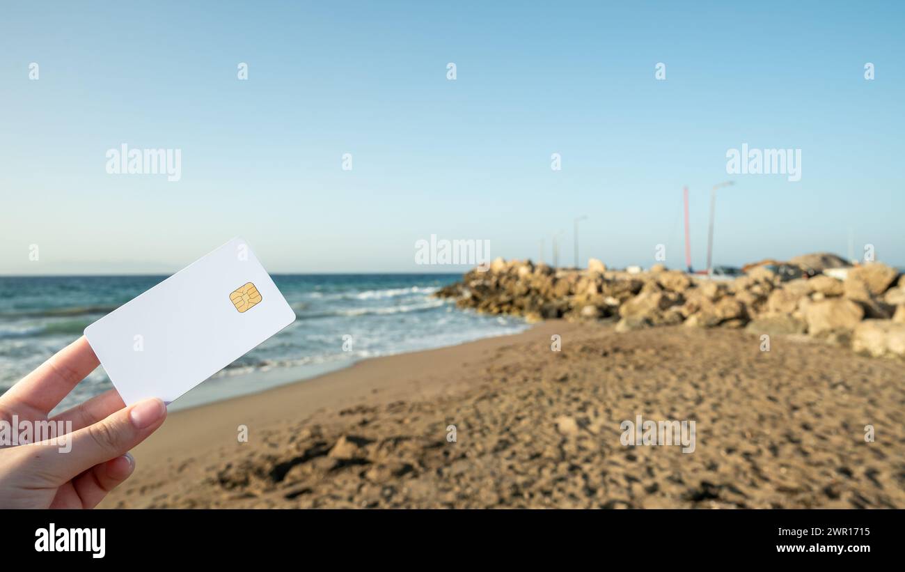 Dans la main d'une femme une carte bancaire blanche sur un fond de plage et de mer. Banque D'Images