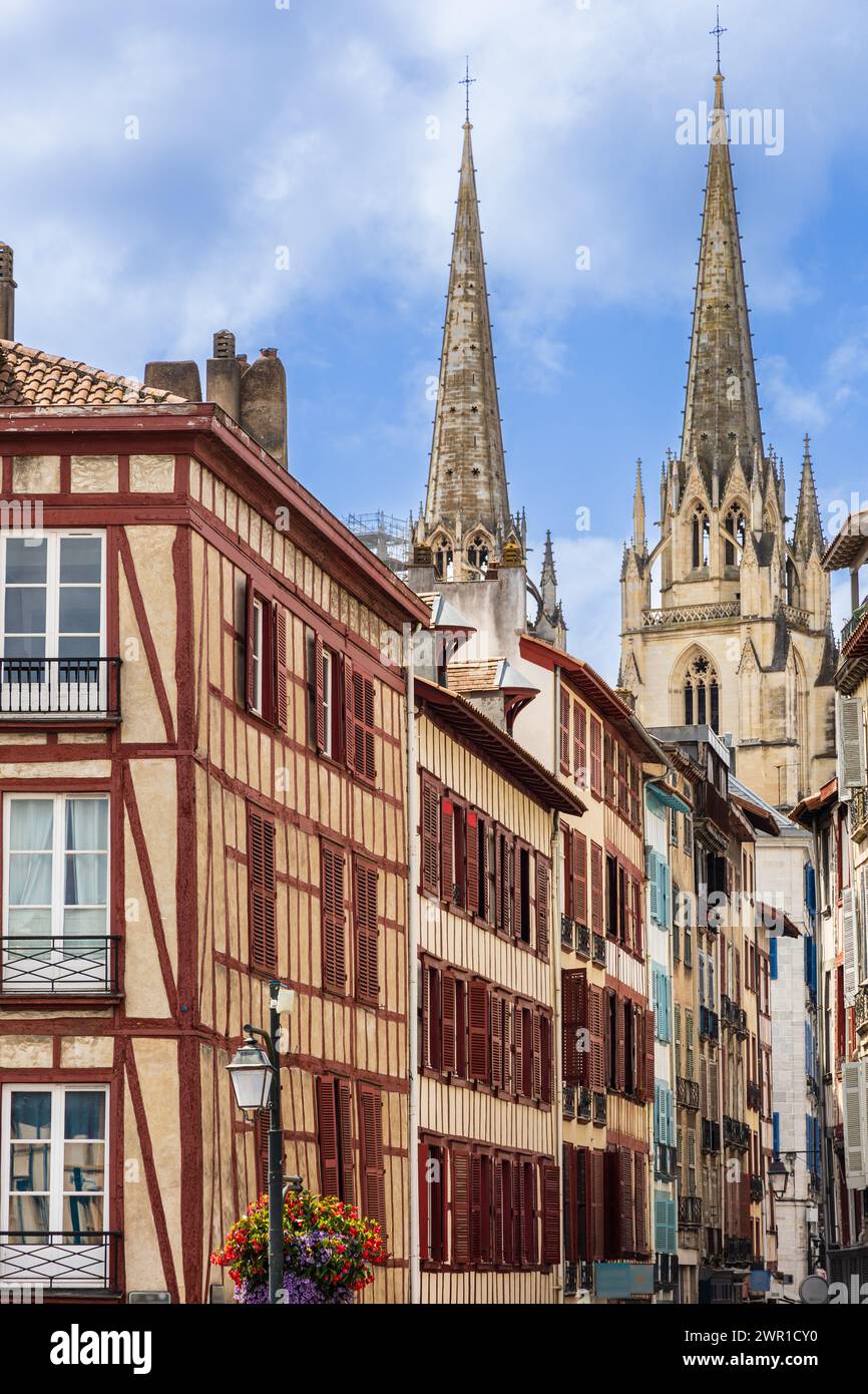 Maisons traditionnelles à colombages avec volets rouges, une rue, et les tours de la cathédrale Sainte-Marie en arrière-plan. Bayonne, France. Banque D'Images