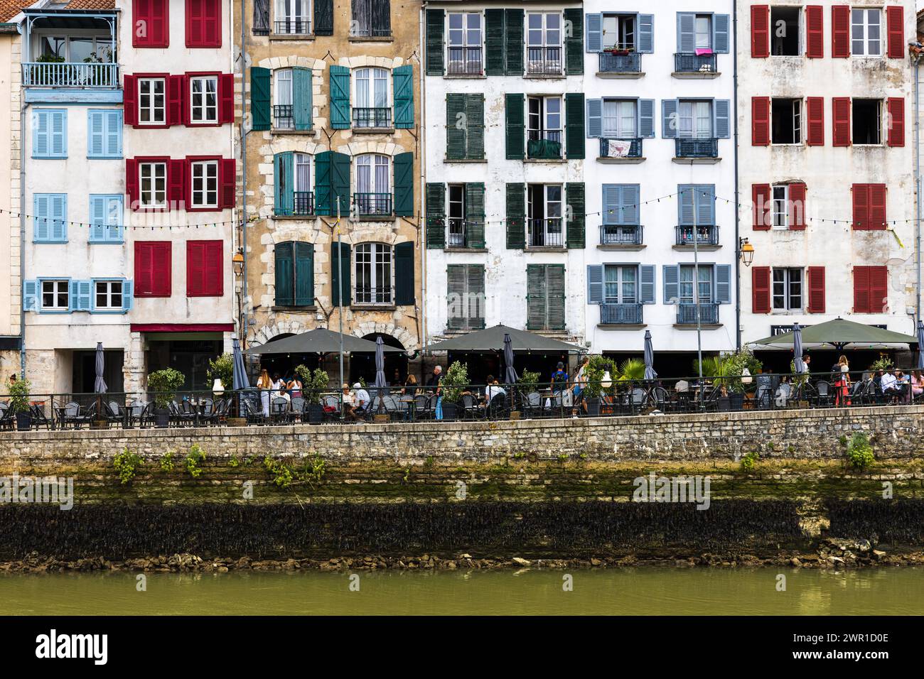 Une vue sur les maisons traditionnelles françaises avec des volets colorés, la rivière Nive, le remblai, et les gens se relaxant dans les cafés de rue. Bayonne, France. Banque D'Images