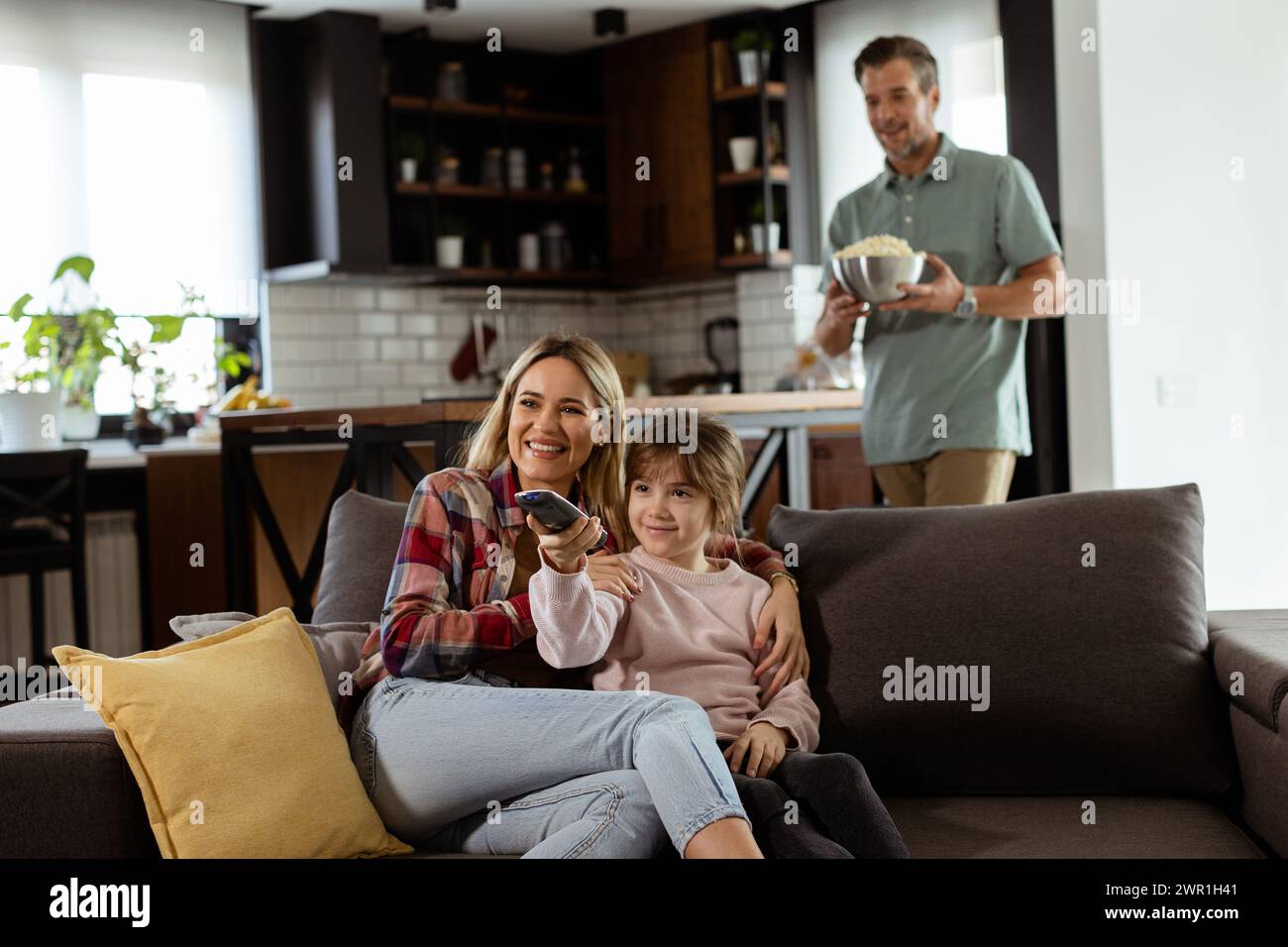 Une famille de trois est confortablement nichée sur un canapé, leurs visages reflétant l'excitation et l'attention comme ils partagent un bol de pop-corn pendant un susp Banque D'Images