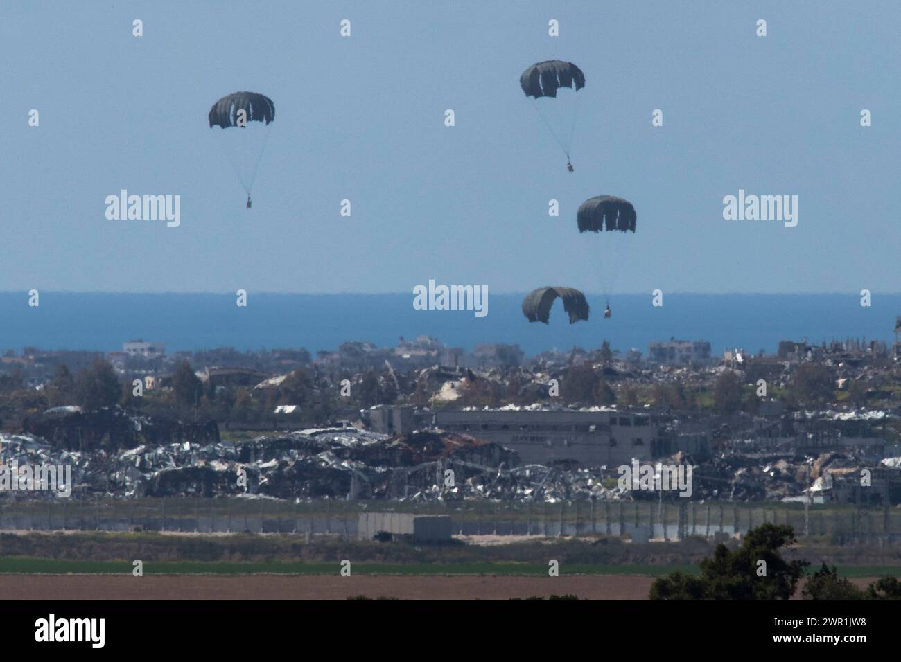 Sud d'Israël, Israël. 10 mars 2024. Ce que l'on pense être un C-130 de l'armée de l'air américaine lâche de l'aide humanitaire en parachute au-dessus du nord de la bande de Gaza vu de l'intérieur du sud d'Israël le 10 mars 2024. Les États-Unis et d'autres pays continuent de distribuer de la nourriture et d'autres fournitures d'aide humanitaire aux Palestiniens dans le besoin dans la bande de Gaza juste avant le début du mois sacré islamique du Ramadan alors que la guerre d'Israël contre le Hamas se poursuit. La mer Méditerranée est vue derrière. Photo de Jim Hollander/UPI crédit : UPI/Alamy Live News Banque D'Images
