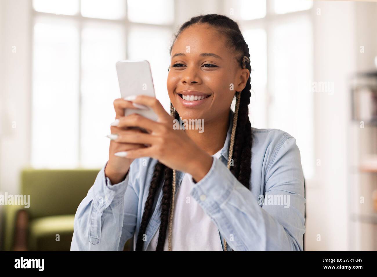 Heureuse adolescente noire appréciant le contenu sur son smartphone Banque D'Images