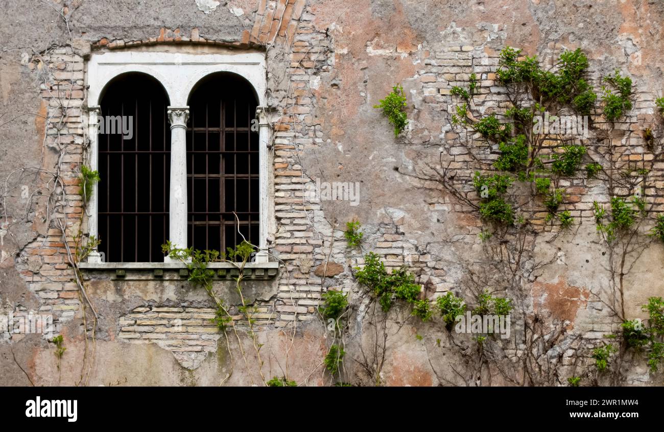 fenêtre altérée et usée avec des grilles métalliques sur un extérieur en brique en ruine, encadrée par de la pierre brute Banque D'Images