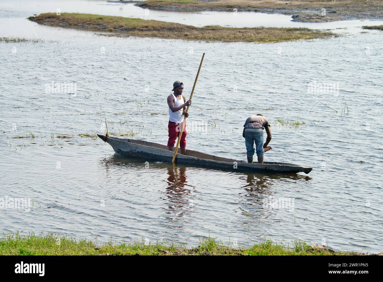 Deux villageois pêchent à partir d'un canot de canot sur un lagon d'une rivière en Afrique ; l'un est en train de frapper le bateau et l'autre est en train de jeter le filet de pêche Banque D'Images