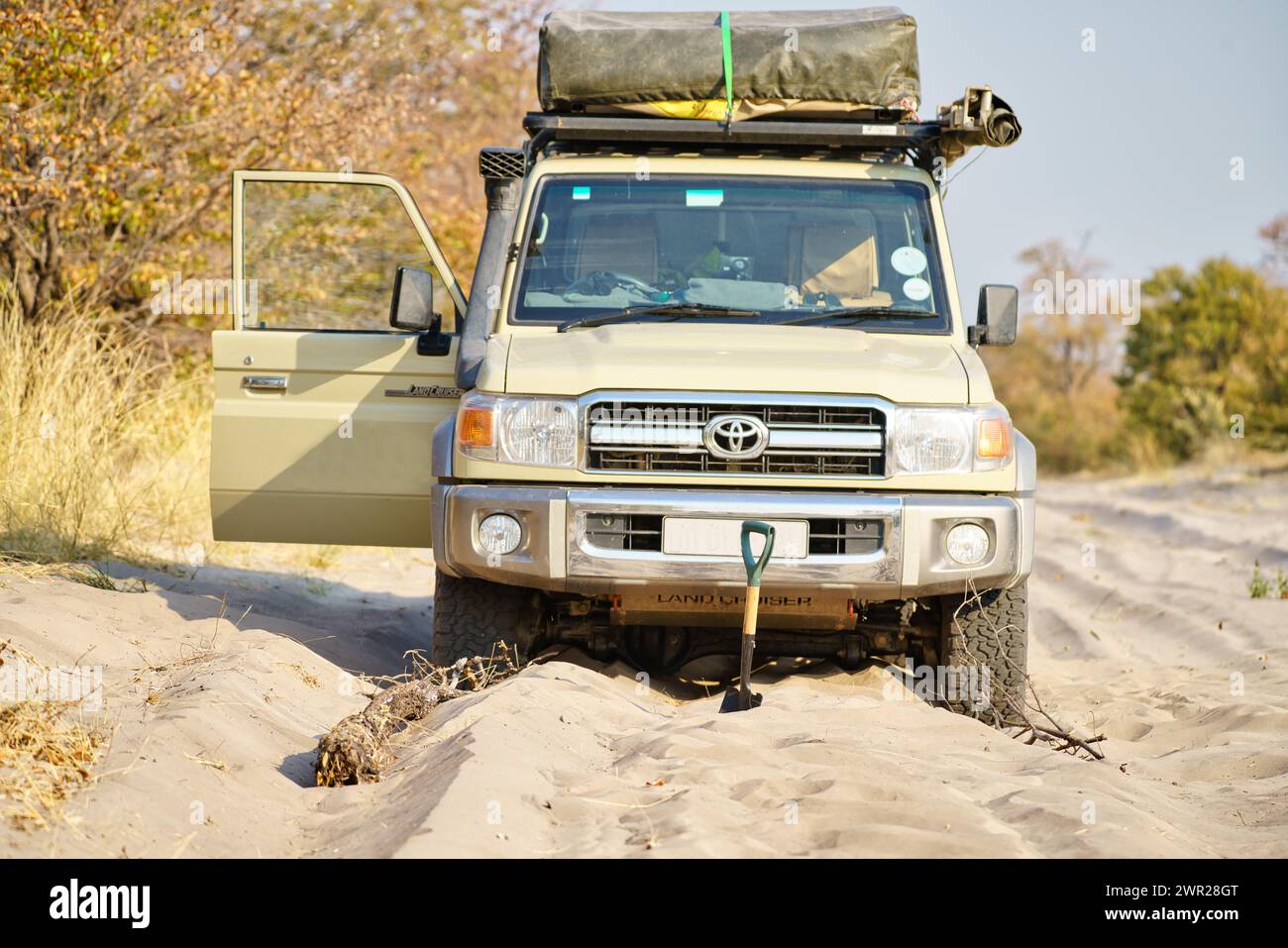 Un véhicule hors route coincé dans le sable profond alors qu'il se déplace sur une route de sable au Botswana. Le véhicule est creusé avec une pelle à sable. Banque D'Images