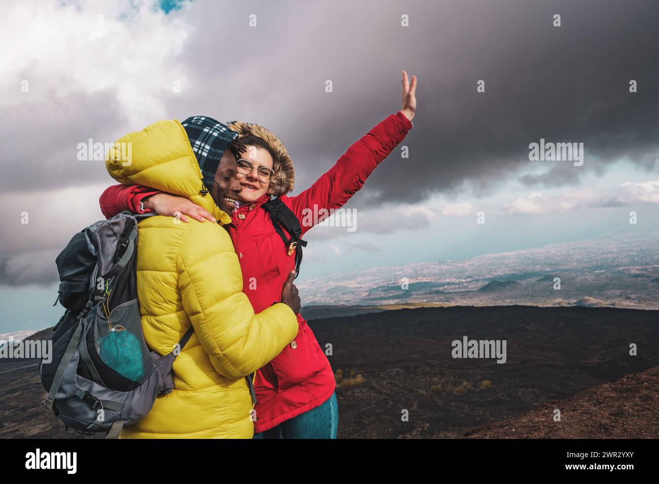 Les randonneurs s'embrassent dans la célébration au sommet de la montagne - moment exaltant de triomphe, avec des vues panoramiques sous un ciel spectaculaire. Banque D'Images