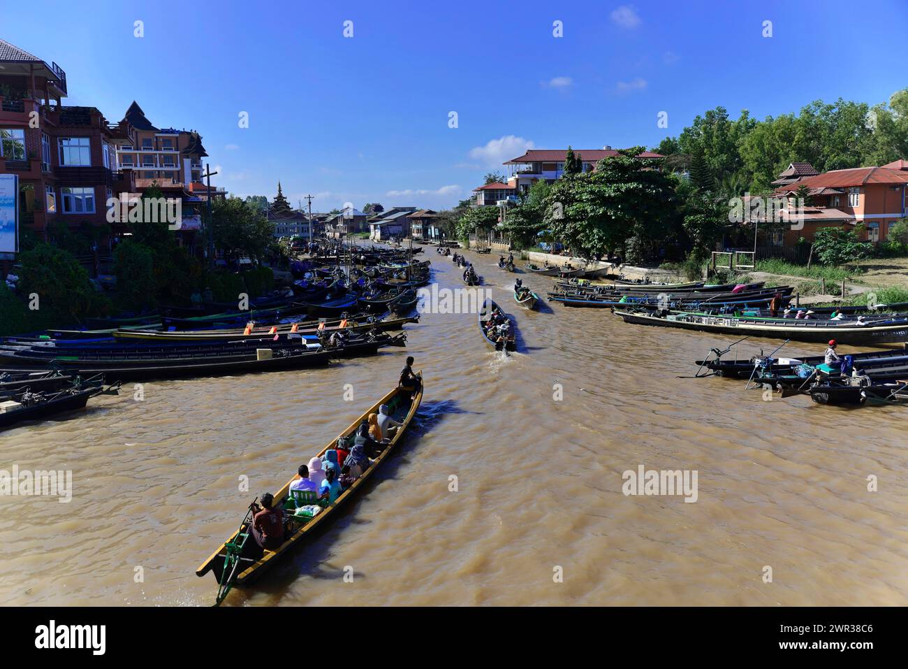 Scène fluviale animée avec des bateaux et un paysage urbain en arrière-plan, Pindaya, lac Inle, Myanmar Banque D'Images