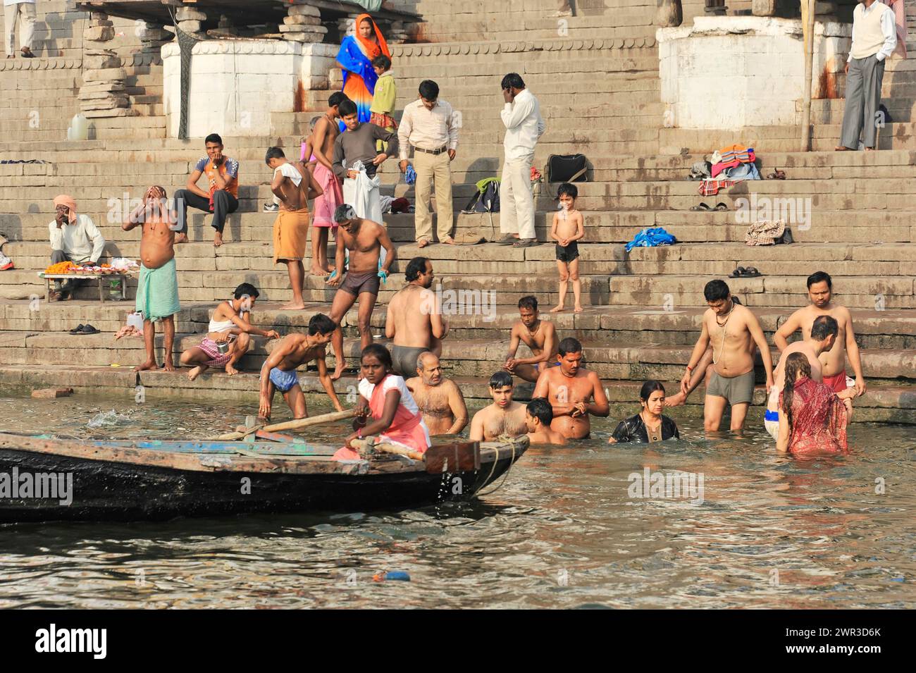 Un bateau passe devant un groupe de personnes se baignant dans l'eau à la rivière Steps, Varanasi, Uttar Pradesh, Inde Banque D'Images