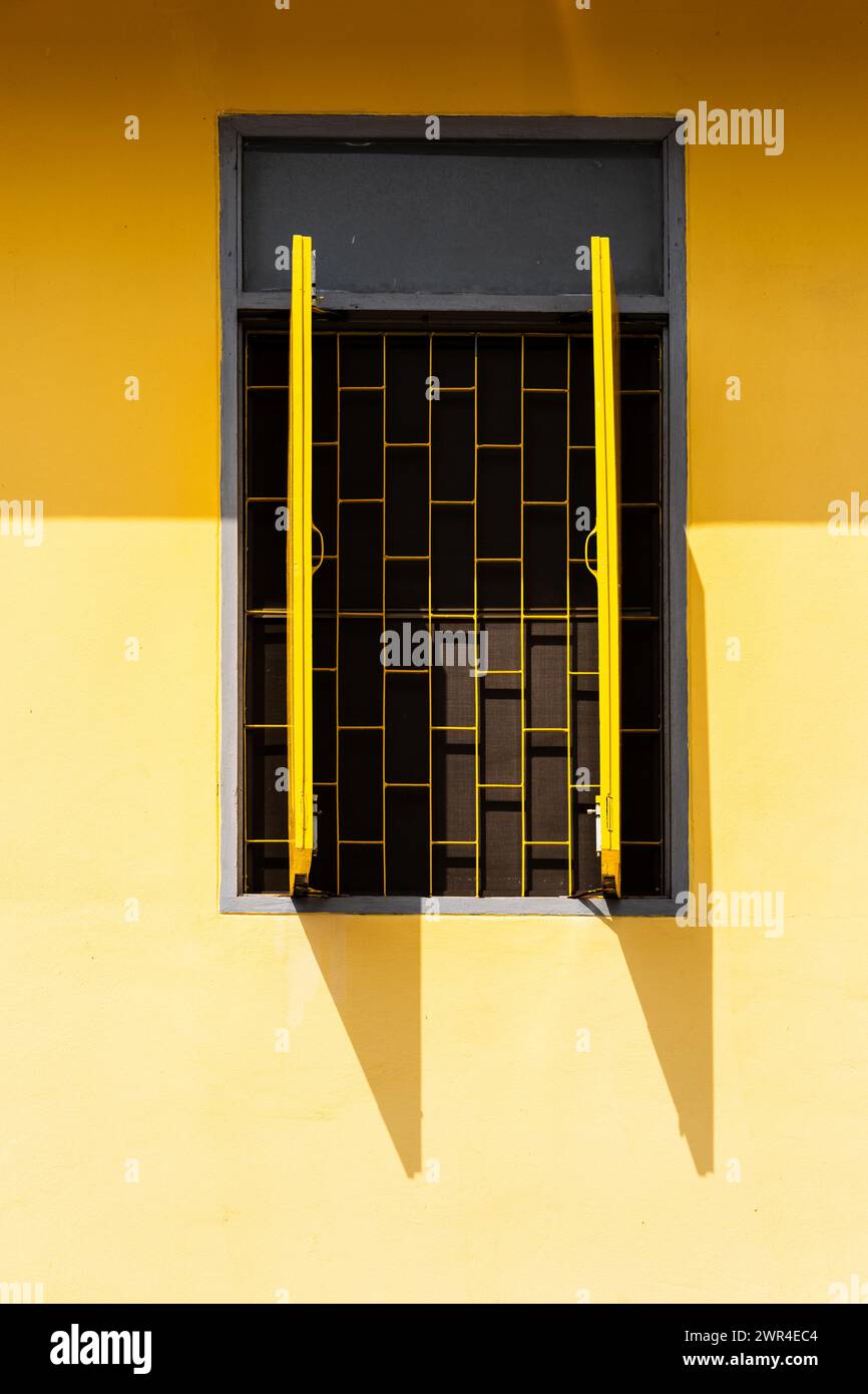 Une fenêtre dans un mur jaune avec des volets jaunes ouverts. Banque D'Images