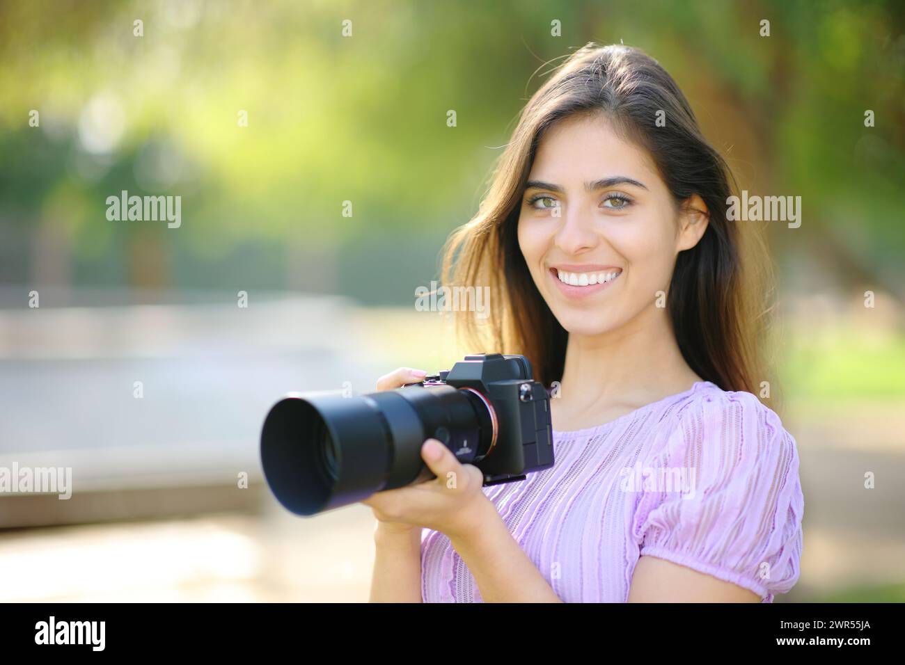 Photographe heureux posant regardant la caméra et tenant sans miroir dans un parc Banque D'Images