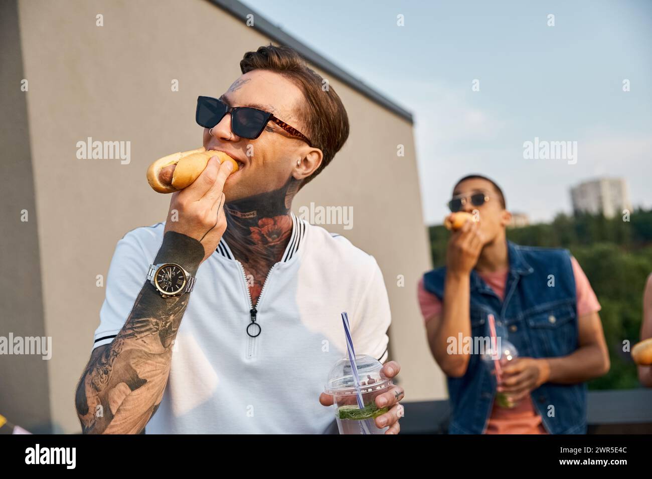 focus sur bel homme avec des tatouages avec son ami afro-américain sur fond manger des hot-dogs Banque D'Images