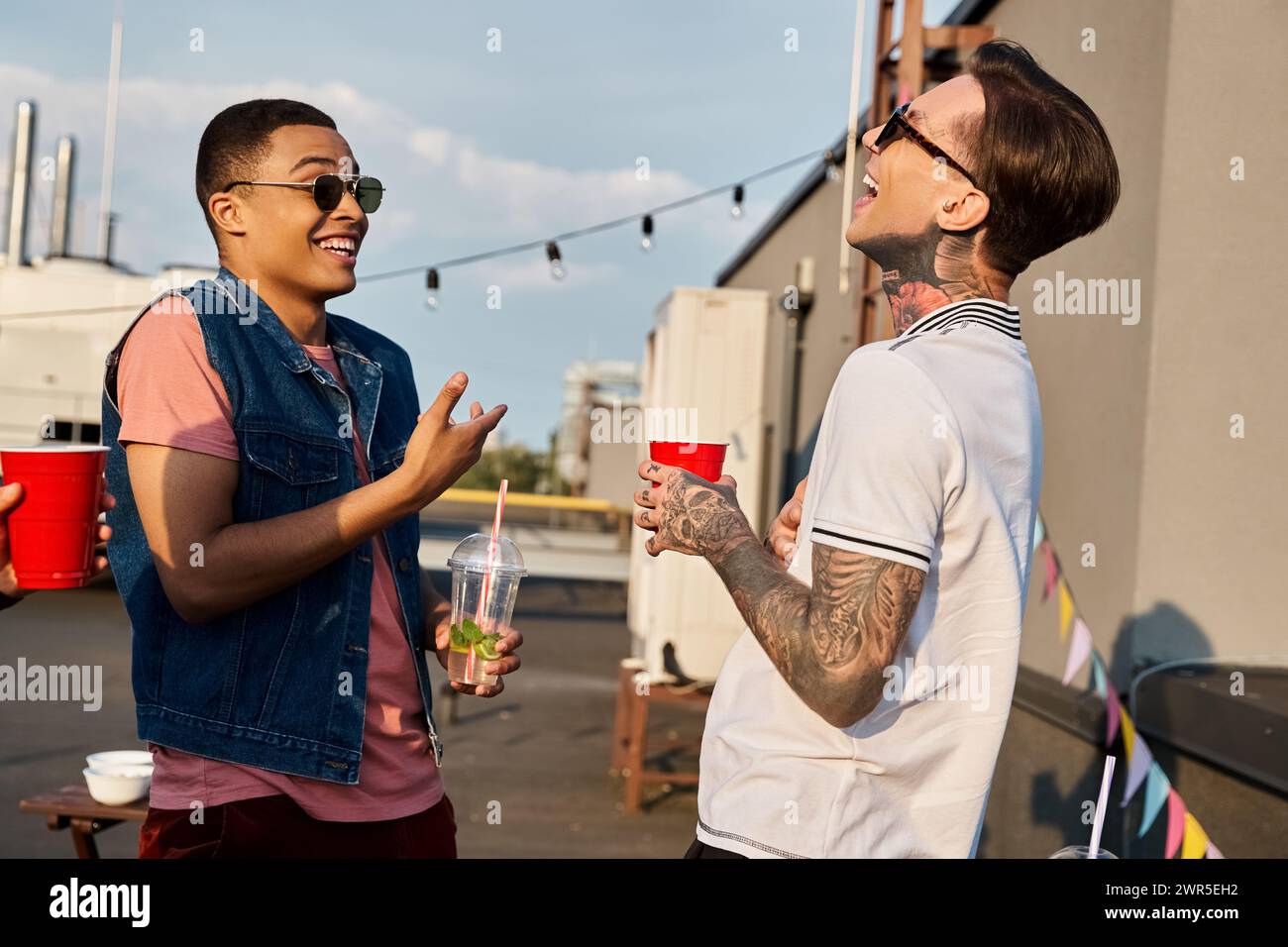 deux amis multiraciaux dans des vêtements décontractés avec des lunettes de soleil s'amusant ensemble à la fête sur le toit Banque D'Images