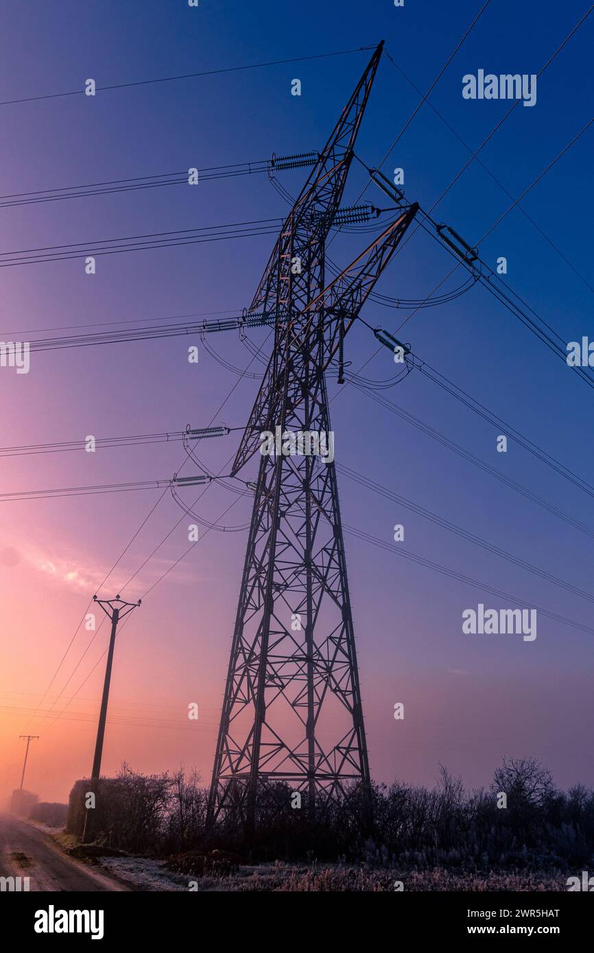 Pylône métallique transportant de l'électricité haute tension avec un ciel bleu et rouge, couleurs de l'aube. France, Europe Banque D'Images