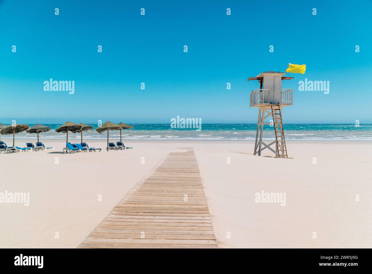Journée ensoleillée à la plage avec tour de sauveteur et parasols Banque D'Images