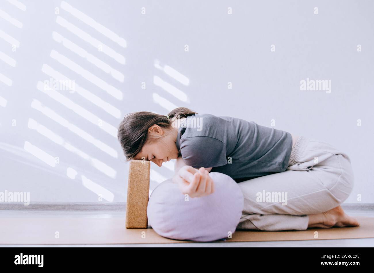 Femme dans des vêtements décontractés faisant le yin yoga bras croisé stretch avec traversin et bloc de liège Banque D'Images