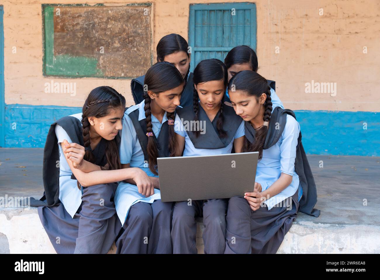 Groupe d'écolières rurales en uniforme assis dans le couloir scolaire travaillant sur ordinateur portable - concept d'éducation numérique Banque D'Images