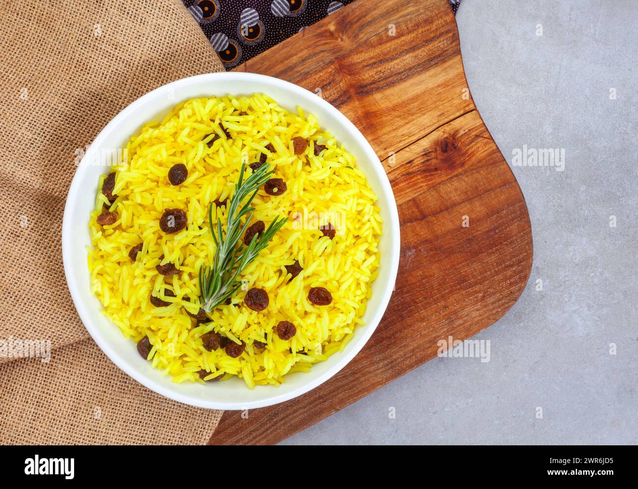 Riz jaune sud-africain traditionnel, fait avec du curcuma et des raisins secs avec garniture de romarin, dans un bol rond avec une planche de bois rustique. Vue de dessus ou plat Banque D'Images