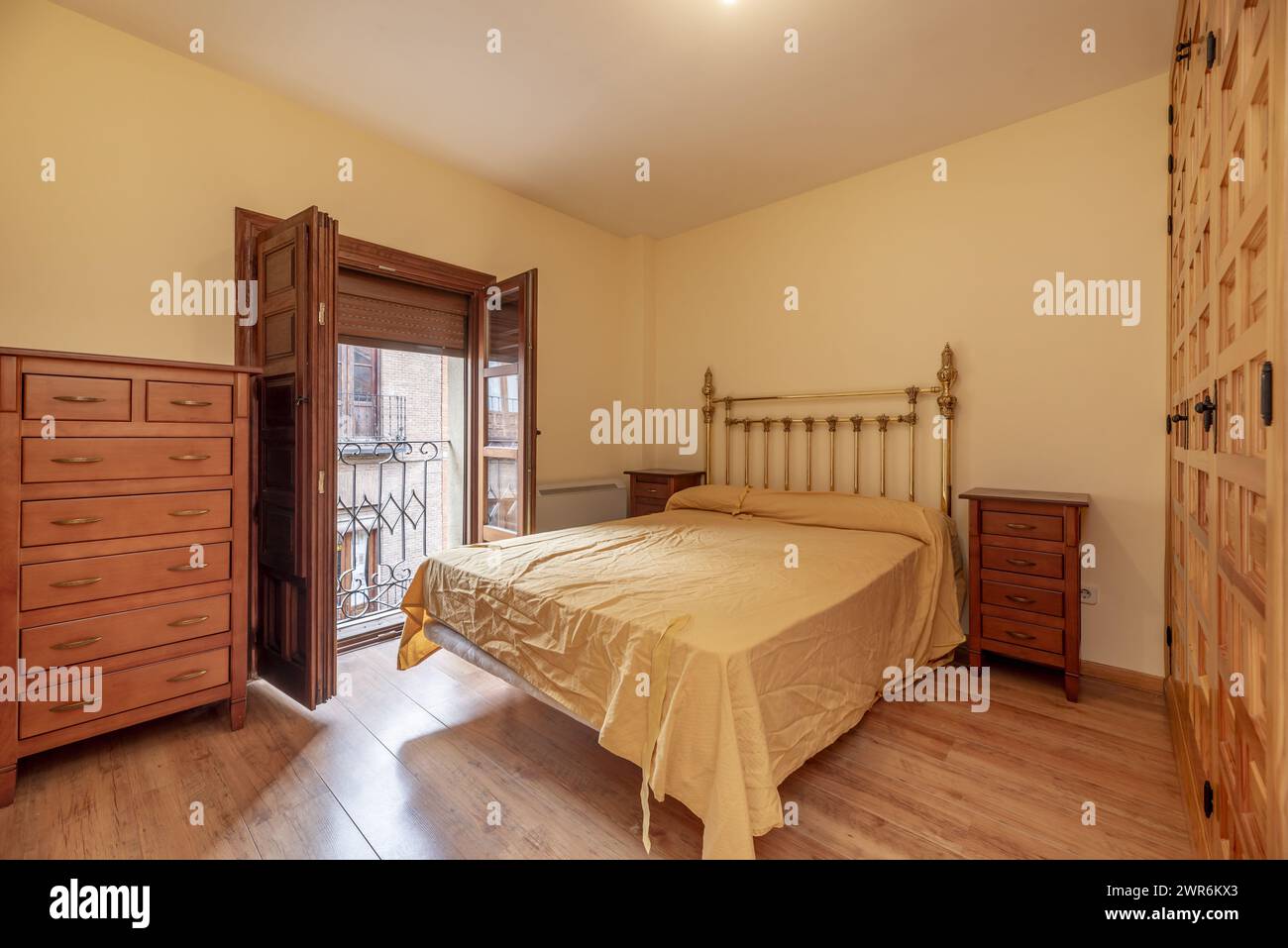 Une chambre avec une porte d'armoire intégrée avec des portes en pin lambrissées de style castillan, un balcon avec des volets en bois et du parquet clair Banque D'Images