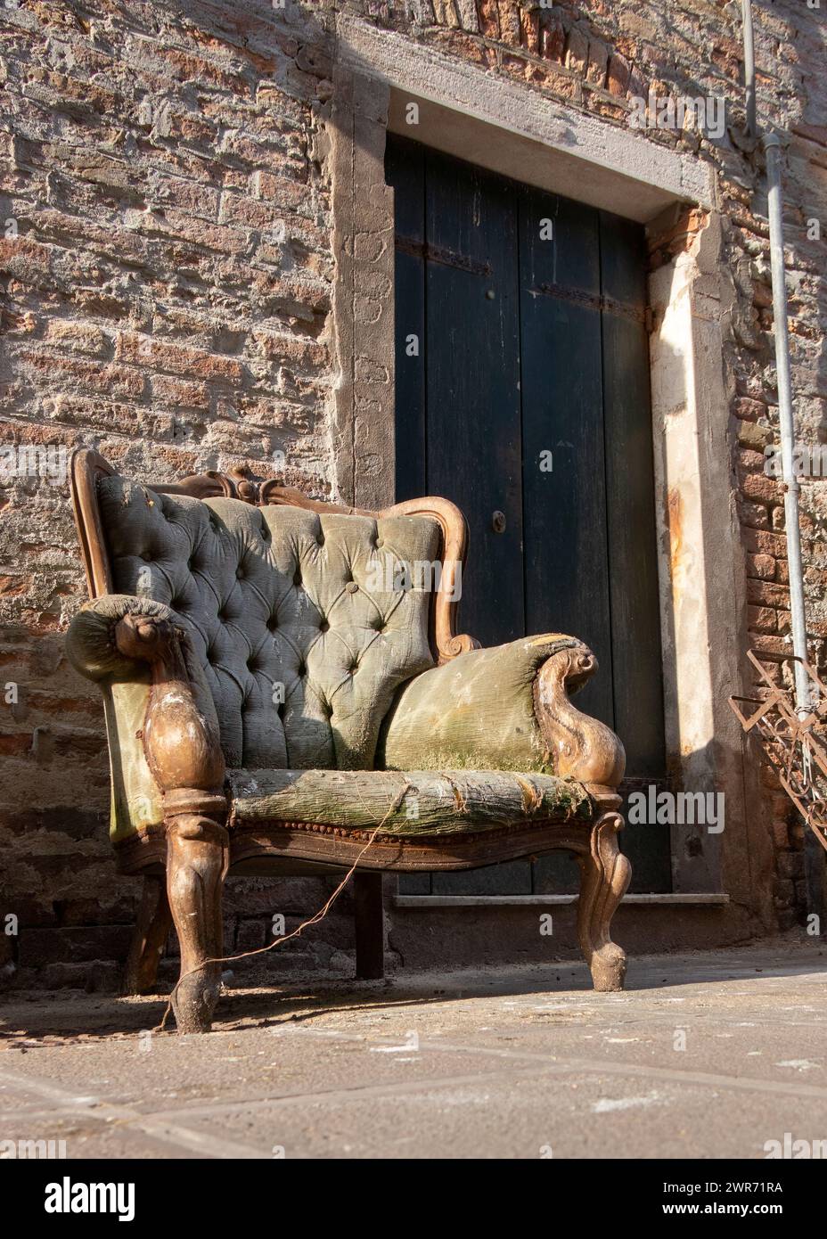 Ancienne chaise verte rembourrée antique vintage délabrée située à l'extérieur d'une porte d'entrée à jeter Chioggia Italie Banque D'Images