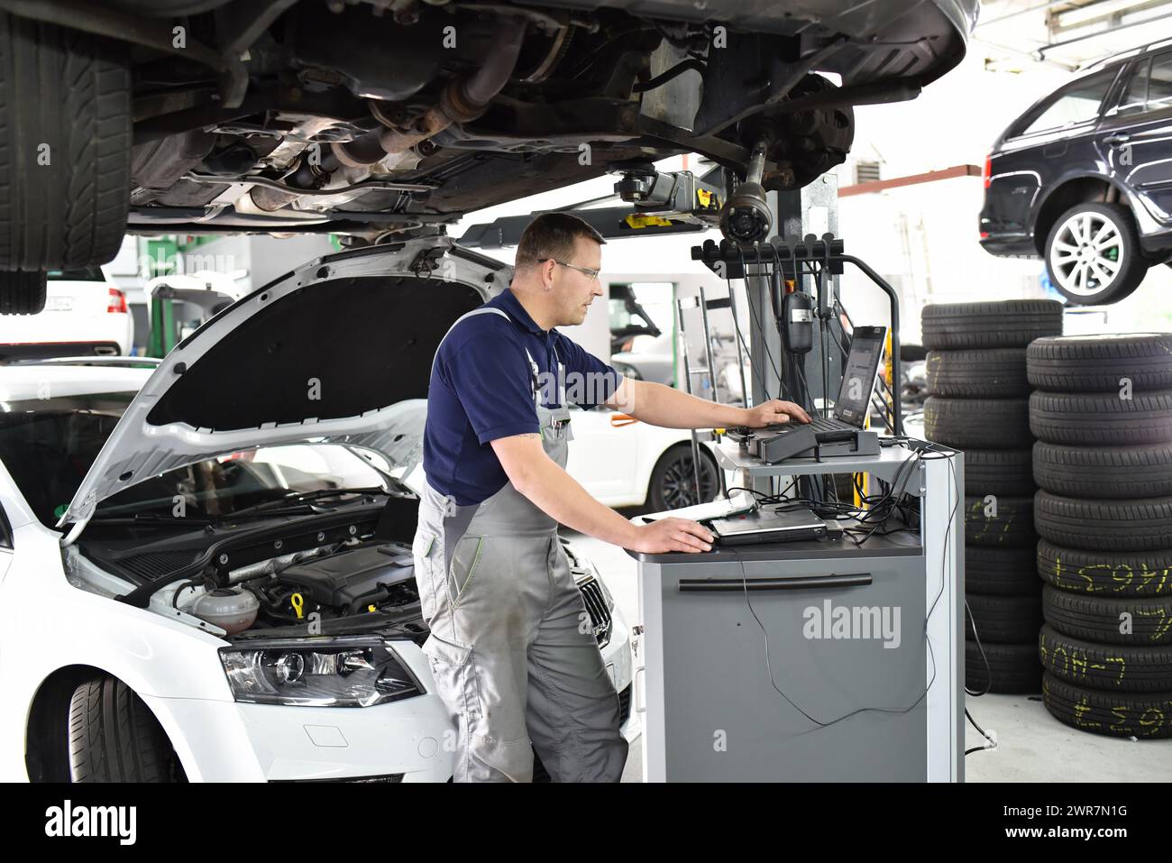 Mécanicien automobile maintient un véhicule avec l'aide d'un ordinateur de diagnostic - La technologie moderne dans l'atelier de réparation de voiture Banque D'Images Mécanicien automobile maintient un véhicule avec l'aide d'un ordinateur de diagnostic - La technologie moderne dans l'atelier de réparation de voiture Banque D'Images