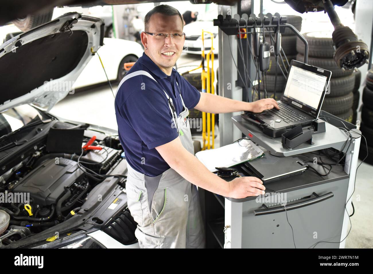 Mécanicien automobile maintient un véhicule avec l'aide d'un ordinateur de diagnostic - La technologie moderne dans l'atelier de réparation de voiture Banque D'Images Mécanicien automobile maintient un véhicule avec l'aide d'un ordinateur de diagnostic - La technologie moderne dans l'atelier de réparation de voiture Banque D'Images