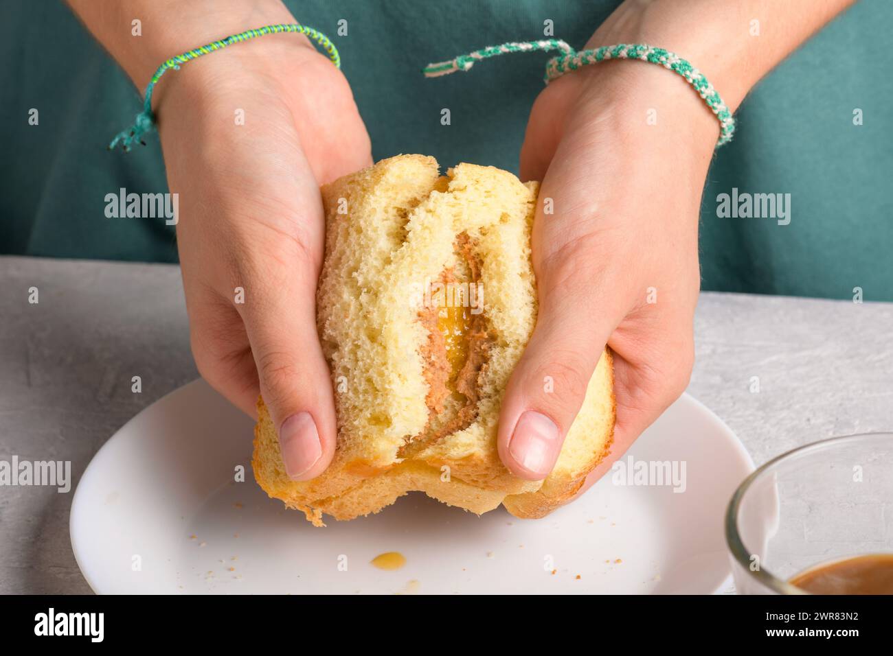 les mains de la femme brisant un sandwich avec du miel et du beurre d'arachide de pain de blé sur une assiette blanche, pour prendre un petit déjeuner, de près. Snack typique, nourriture Banque D'Images