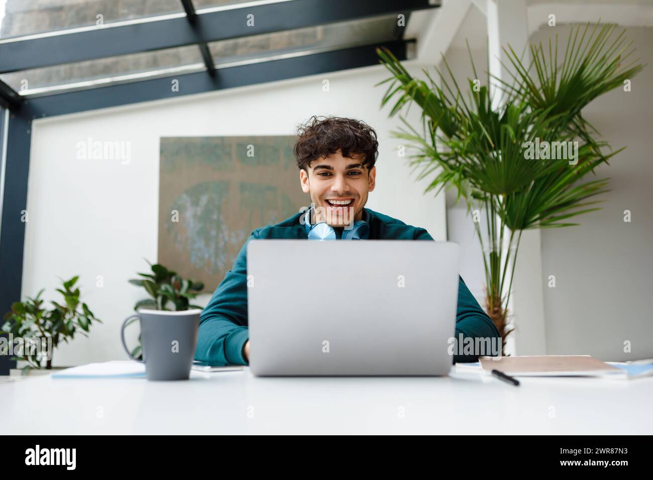 Homme freelance riant avec des écouteurs à l'ordinateur portable Banque D'Images