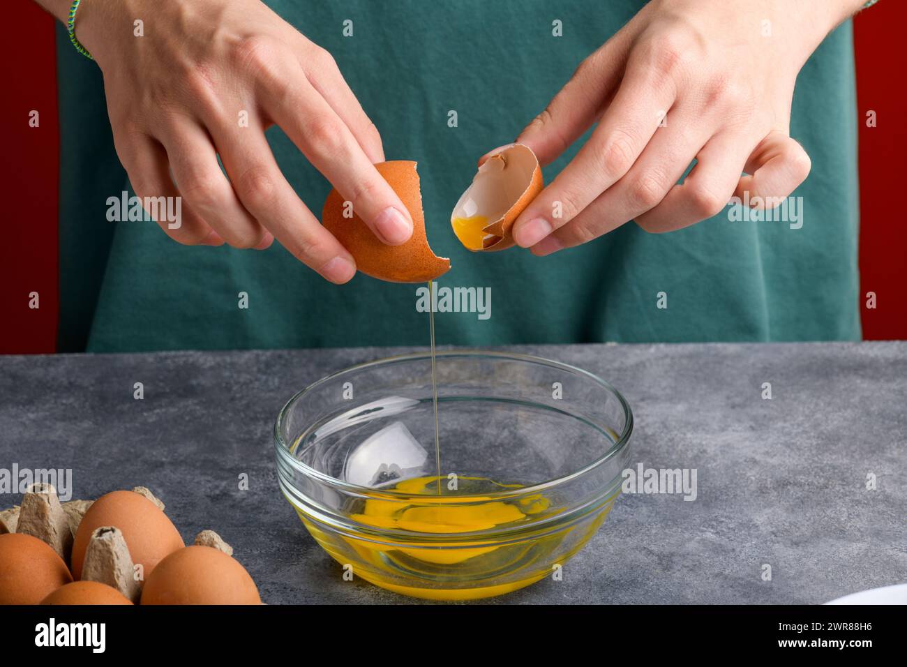 La main d'une femme tenant les coquilles d'oeuf brassé dans un bol en verre clair dans la table de cuisine grise, le processus de cuisson, les oeufs frais dans le bol Banque D'Images