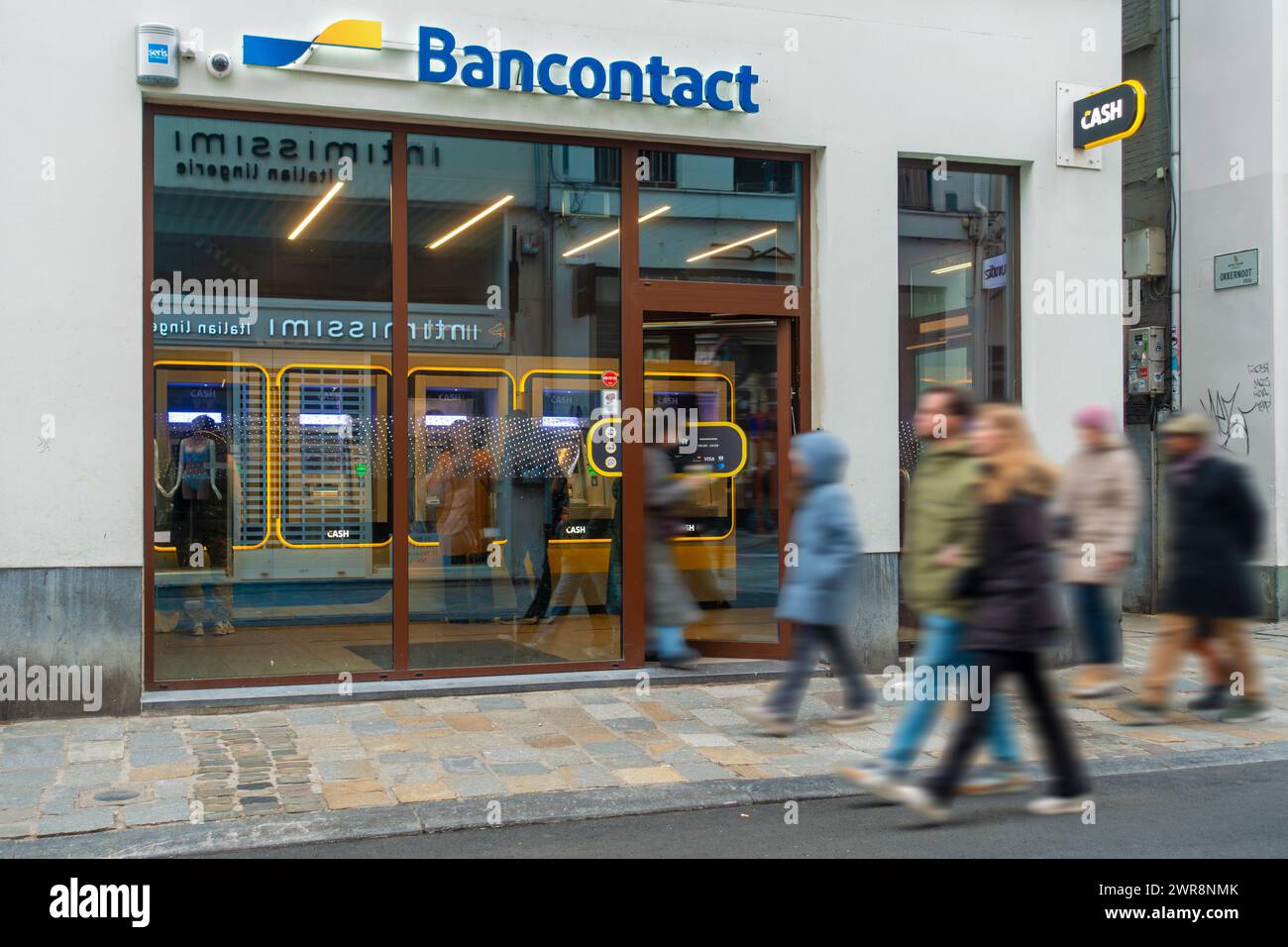 Les acheteurs passant devant le distributeur automatique de billets intérieur du point de TRÉSORERIE Bancontact neutre de banque dans la rue commerçante de la ville Gand / Gand, Flandre orientale, Belgique Banque D'Images