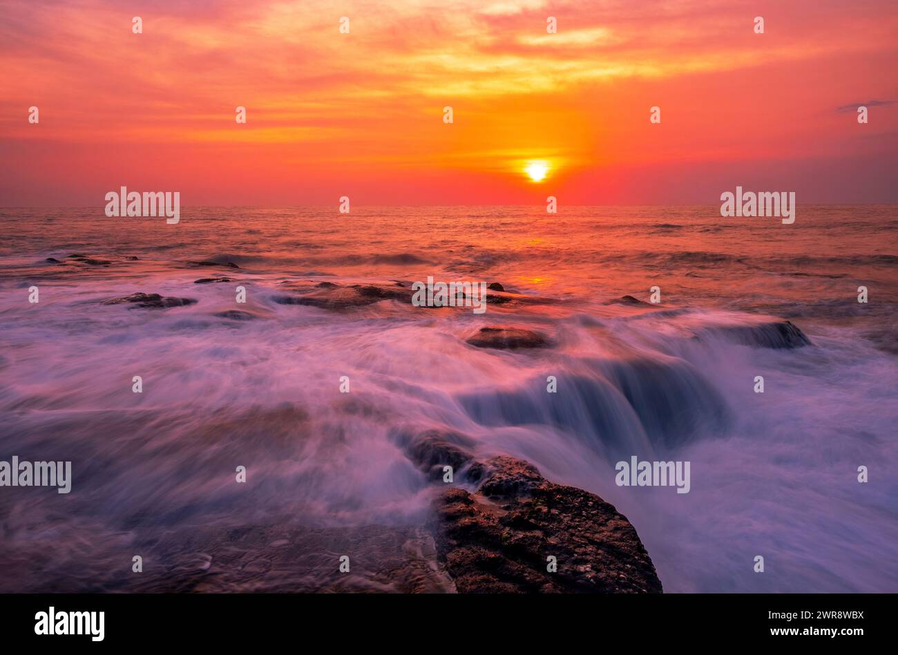 Atmosphère enchanteresse de la mer surf au coucher du soleil ; les vagues se répandent sur un rivage rocheux avec un effet de flou obtenu en utilisant une longue exposition Banque D'Images