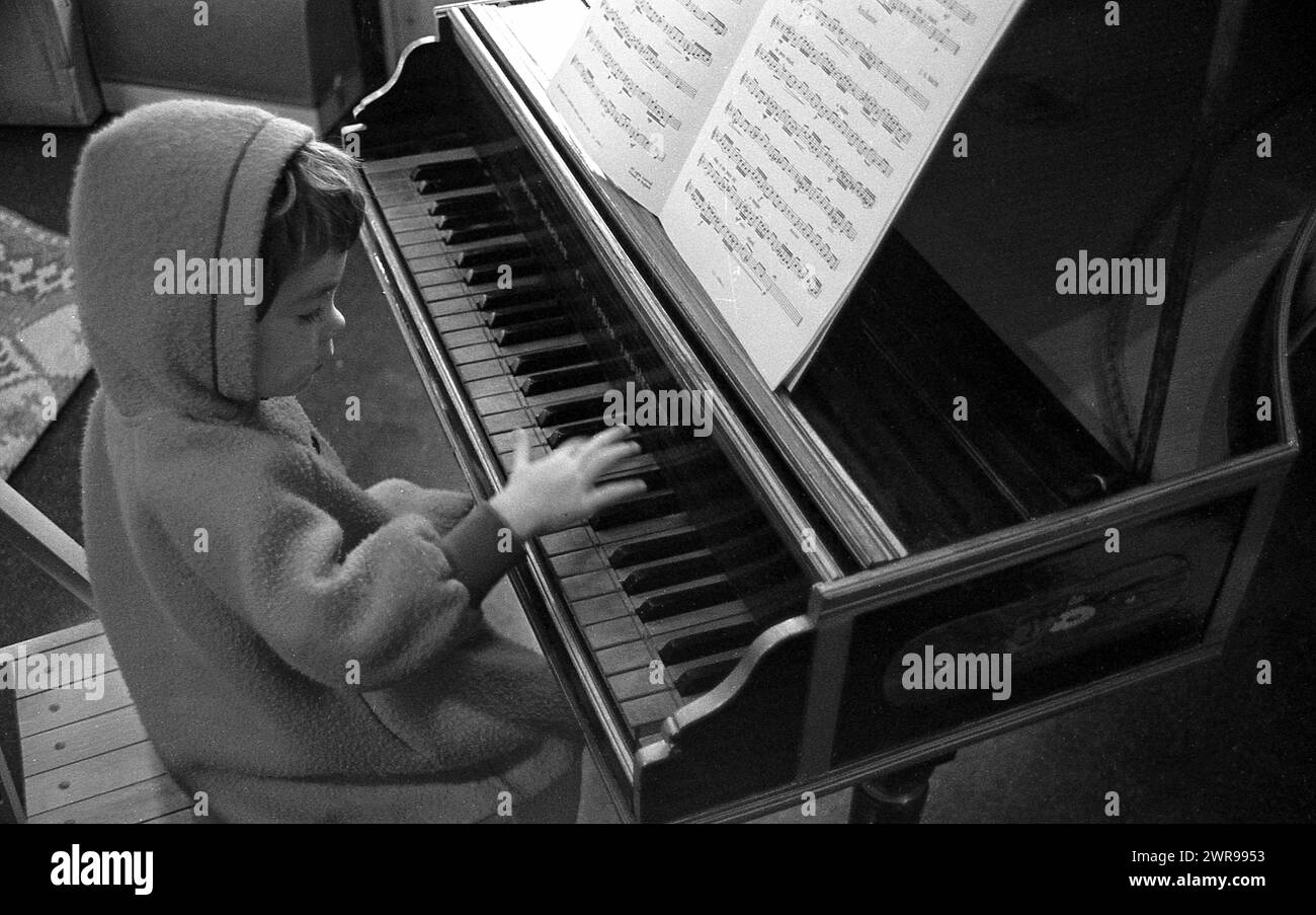 Années 1960, historique, un petit garçon en polaire à capuche stting à un piano bébé pressant une touche, Angleterre, Royaume-Uni. Banque D'Images