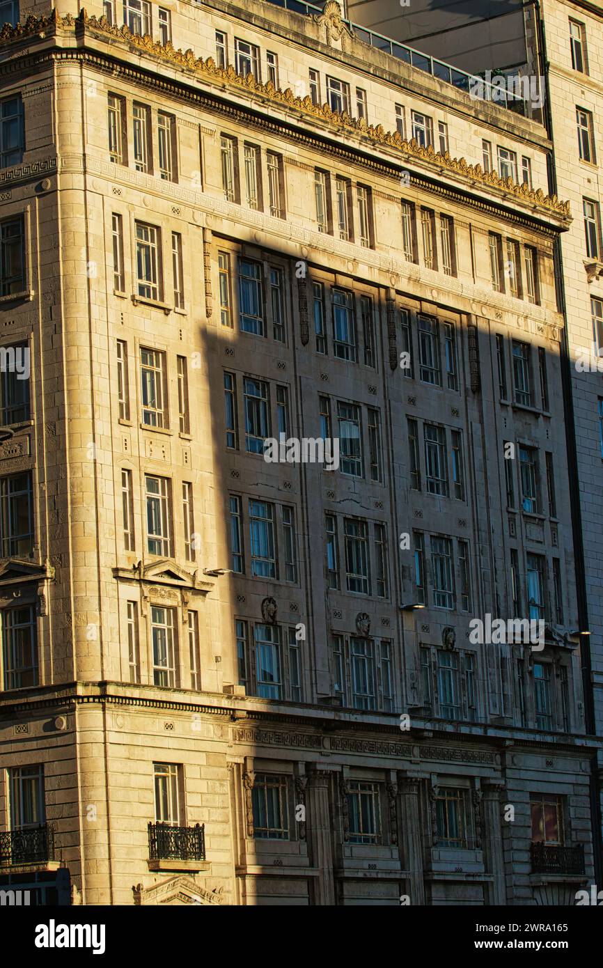 La lumière du soleil projette des ombres sur une façade de bâtiment urbain classique pendant l'heure d'or, mettant en évidence les détails architecturaux à Liverpool, au Royaume-Uni. Banque D'Images