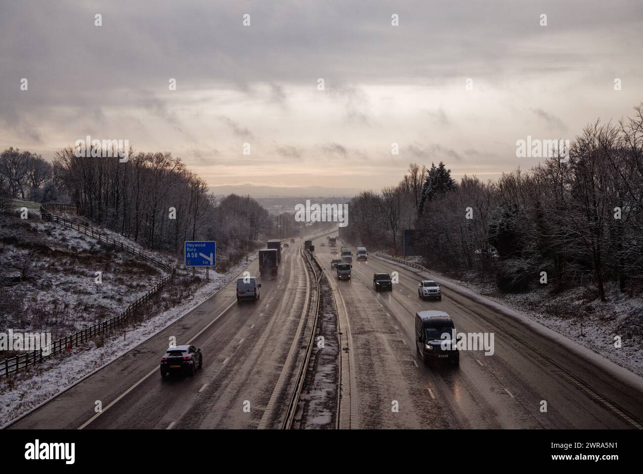 Véhicules circulant sur une autoroute glacée dans un cadre boisé enneigé sur la M56, Bury, Greater Manchester. Banque D'Images