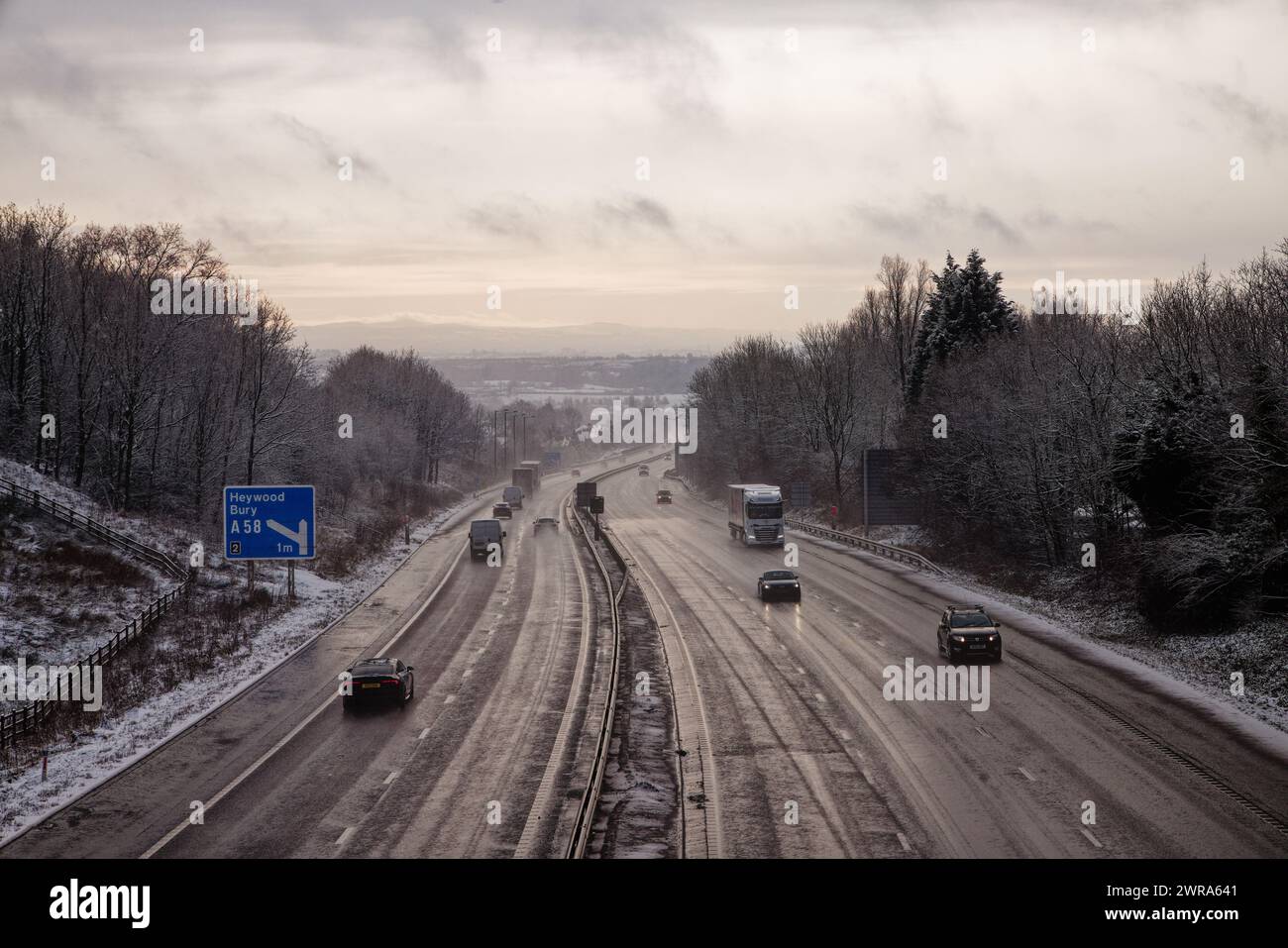 Une autoroute hivernale à travers les bois avec des véhicules sur la route glacée sur la M56, Bury, Greater Manchester. Banque D'Images