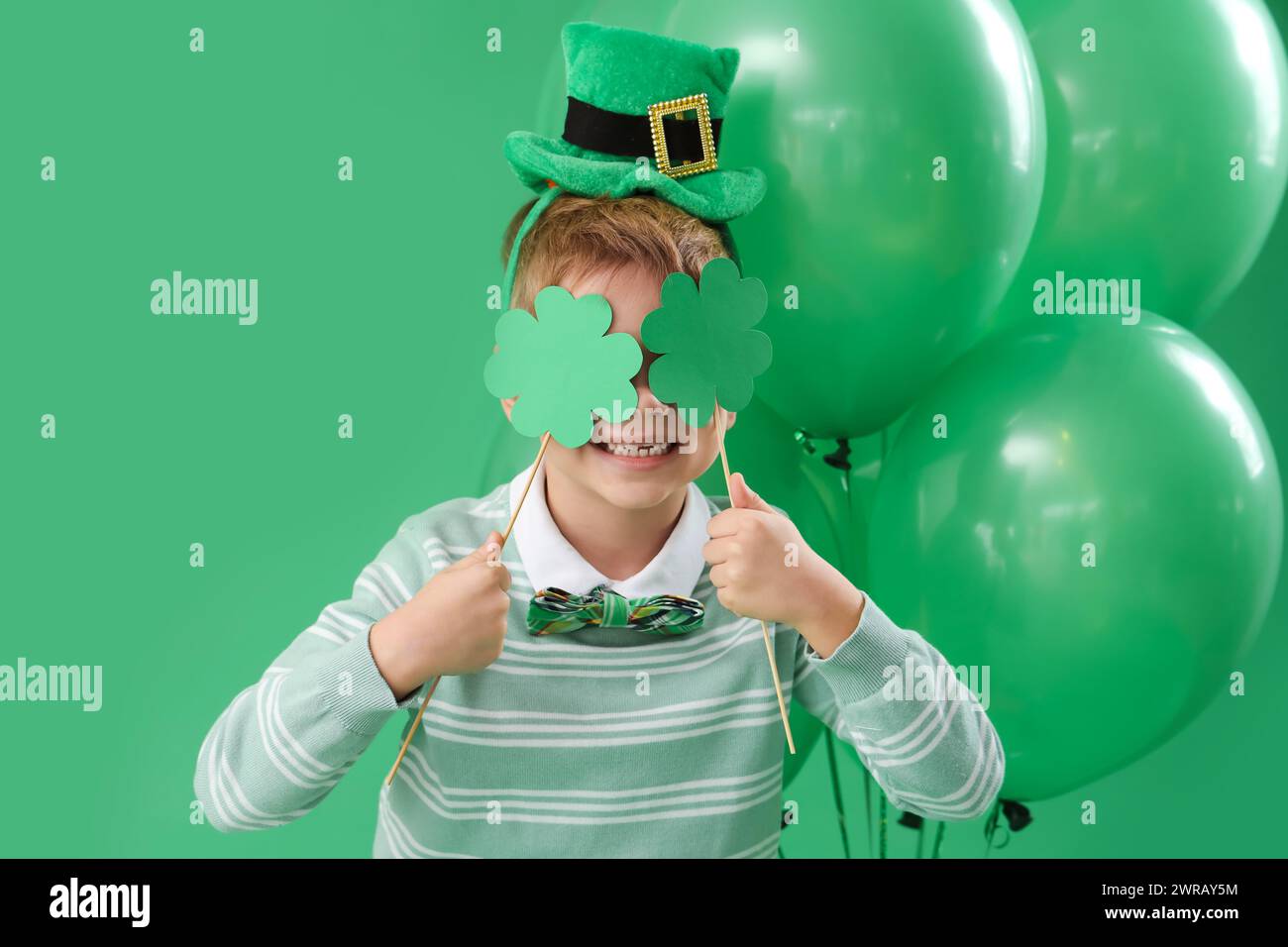 Mignon petit garçon avec chapeau de leprechaun, trèfles et ballons sur fond vert. Prog Célébration de la fête de Patrick Banque D'Images